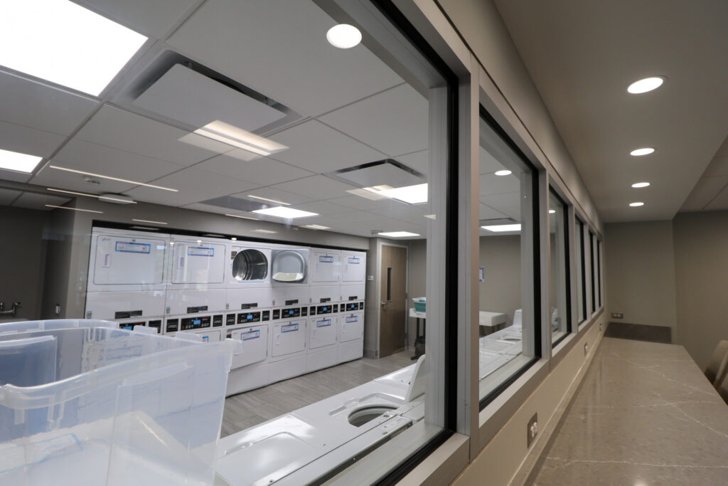 A view of the laundry room with several dryer machines stacked on top of each other, and a line of dryers under a window.